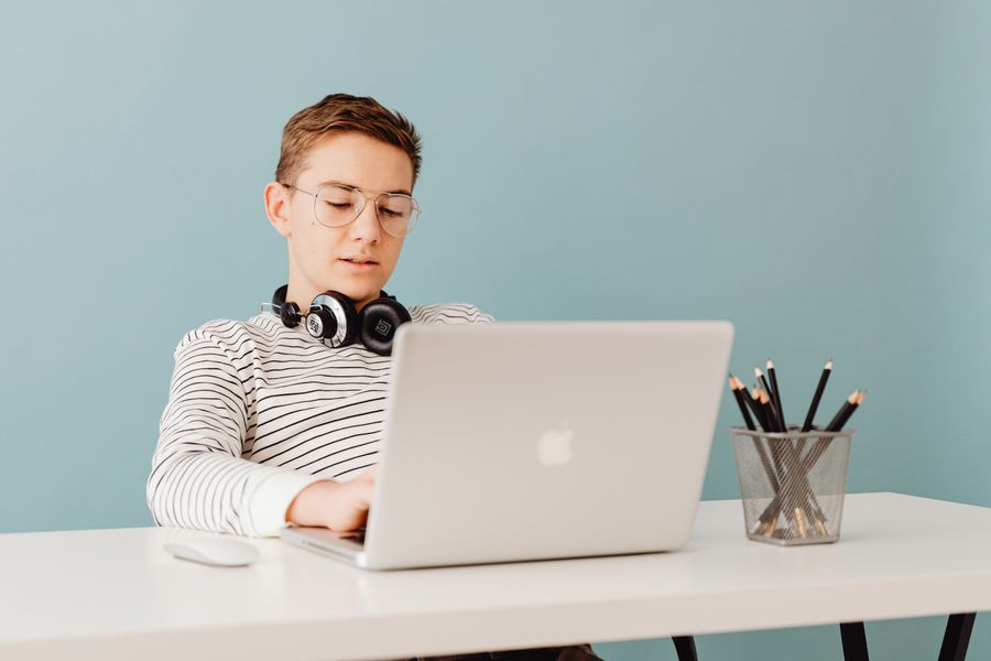 A student with headphones round his neck working on a laptop at a desk.